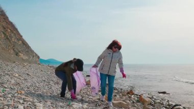 Kadınlar okyanus kirliliğini azaltmak için plastik atıklar ve diğer çöpleri toplayarak kirli bir plajı temizlemeye gönüllü oluyorlar. Dünya Günü ve çevresel farkındalık kavramı. Tam boy çekim.