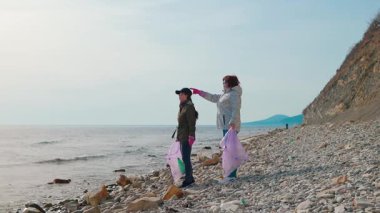 İki kadın aktivist bir plaj temizliğine katılıyor, kirlilikle savaşmak ve vahşi yaşamı korumak için plastik ve diğer atıkları topluyorlar. Çevresel farkındalık ve deniz koruma kavramı. Yan görünüm