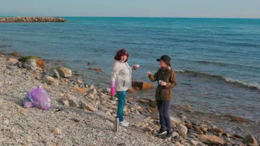 İki kadın, kirlenmiş bir plajı temizlemek ve okyanusu plastik atıklardan korumak için gönüllü olarak çalışıyor. Gönüllüler bir fren yapıp çay içsin. Geniş açı