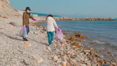 İki kadın, okyanus kirliliğini önleme ve deniz yaşamını kurtarma amaçlı bir çevre girişimi kapsamında deniz kıyısı boyunca plastik atık topluyor. İnsanlar Dünya Günü için plajı temizliyor..