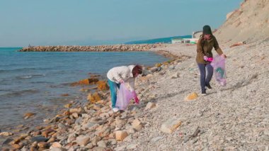 Kadın gönüllüler kıyı boyunca kum ve kayalardan çöp toplayarak plastik kirliliğini önlemek ve çevresel sorumluluk bilincini artırmak için çalışıyorlar. Dünya Günü temizlik olayı. Geniş açı.