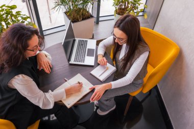 Kadınlar fırlatma varlıklarını koordine ederken espresso yudumlarken rahat bir ortam, esneklik ve hazırlık kavramı. Üst görünüm.