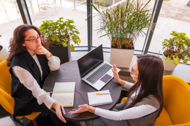 İş odaklı kadınlar, enerjik bir kafe olan çevik takım çalışması konseptinde içki içerken proje zaman çizelgelerini sıralıyorlar. Üst görünüm.