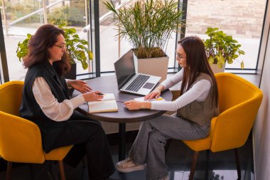 İki genç kadın, yaklaşan girişim, girişimcilik ve yaratıcı strateji kavramları hakkında fikir alışverişinde bulunurken ofis yemeği devam ediyor. Orta çekim.