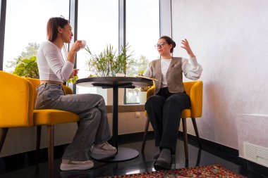 Dinamik kadın girişimciler cappuccino içerken fikirlerini paylaşıyorlar. Küçük işletme büyümesi ve dijital varlık kavramı. Alt görünüm.