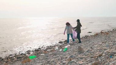 İki çevreci, kirlenmiş bir plajı, vahşi yaşamı korumak ve sahili restore etmek için plastik ve diğer döküntüleri toplayarak temizliyor. Okyanus temizliği ve sorumlu imha kavramı. Geniş açı