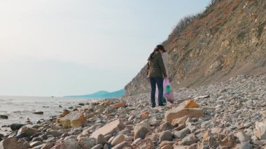 İki aktivist kirlenmiş bir kıyı şeridini temizleyip çevresel hasarı azaltmak için plastik atıkları topluyorlar. Gönüllüler doğa yenilenmesi ve deniz ekosistemi korunumu için harekete geçtiler. Arka plan