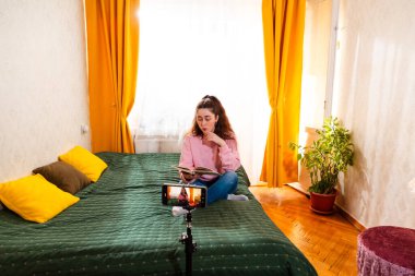 Yatağında video bloğu çeken dijital kadın yaratıcı, çevrimiçi iş hakkında bilgi paylaşmak için tripodun üzerinde akıllı telefon kullanıyor. Geniş açı.