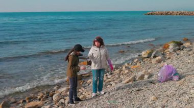 İki aktivist, uzak bir sahilde atık toplamak ve plastik kirliliğinin tehlikeleri hakkında farkındalık yaratmak için çalışıyor. Kadınlar bir fren yapar ve çay içerler. Tam boy çekim.