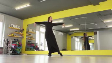 Sağlıklı enerjik genç beyaz kadın spor salonunda dans çalışmasına katılıyor. Esneklik, esneklik ve atletizm eğitimi ve refahı için kararlılık gösteriyor. Düşük açı, geniş açı..