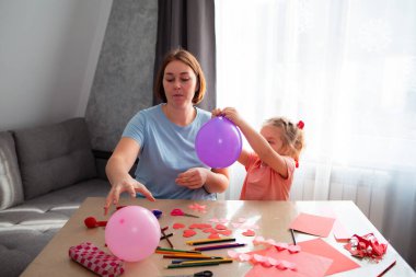 Genç beyaz anne ve küçük kızının balonları şişirmesi ve tatil için dekorasyon yapmasının en güzel manzarası. Mutlu bir aile. Anneler Günü kavramı.