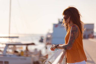 Geminin korkuluklarına dayanan dövmeleri olan güzel, bronzlaşmış genç bir kadın. Uzayı kopyala Deniz gezisi ve yaz tatili. Özgürlük kavramı.