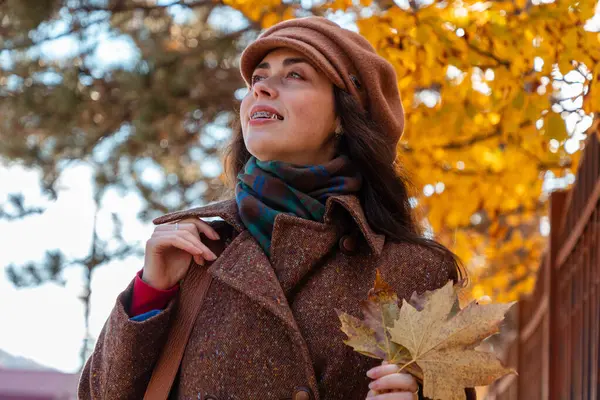 Paltolu güzel beyaz bir kadının sonbahar günü şehir caddesinde sarı yapraklar tutarken görüntüsü. Yaşam tarzı ve şehir hayatı.