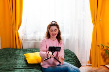 Yatakta oturup sosyal medya kanalı için ilgi çekici bir video çeken coşkulu içerik yaratıcısının portresi.