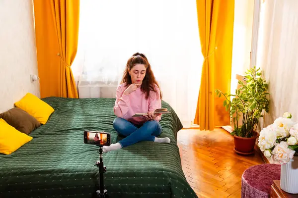 Sosyal medya etkileyicisi yatakta oturup takipçileri için online başarı ve içerik oluşturma hakkında bir video kaydediyor. Geniş açı.