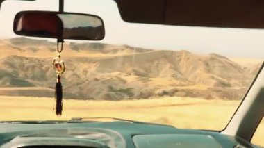 Güneşli, kuru bozkır manzarası ve seyrek savana bitkisi hareket halindeki bir arabanın içinden görülüyor, seyahat özgürlüğü, mesafe ve sonsuz kırsal yolların ritmini çağrıştırıyor. El çekimi..