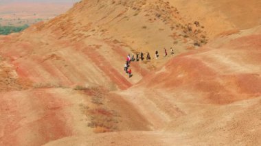 Çöl yürüyüşü sırasında kuru tepelerde yürüyen çeşitli bin yıllık turist grupları, yaz yolculuğunun ve uzak doğal ortamlarda açık hava fitness müsabakalarının keyfini çıkarıyorlar. Geniş açı.