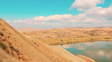 Bakır renkli kil tepeler ve canlı bir gökyüzü altında kayalık Gürcistan platoları arasında uzanan sakin dağ gölü, sakin doğayı, keşfi ve uzak seyahat noktalarını sembolize eder. Çekim.