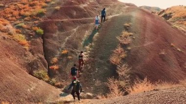 19.10.2024, Tiflis, Georgia. Uzak çöl yolundaki tozlu, altın tepelerde yokuş yukarı yürüyen maceraperest turistler yüksek enerjili yaz gezilerinde birlikte egzotik arazileri keşfediyorlar. Geniş açılı çekim.