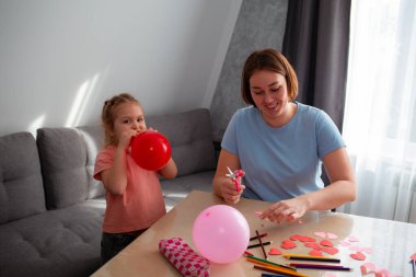 Beyaz tenli genç anne ve küçük kızının balonları şişirmesi ve Anneler Günü için süslemeler yapması. Mutlu aile tatilleri..