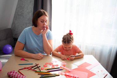 Genç anaokulu öğretmeninin orta fotoğrafı bir kıza tatil için kartpostal çizmeyi öğretiyor..