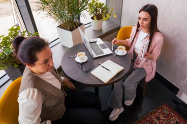 İki genç Kafkasyalı girişimci, büyüyen bir iş için dijital pazarlama stratejileri ve takım çalışması üzerinde çalışarak, modaya uygun bir kafede verimli bir toplantı yapıyorlar. Üst görünüm.