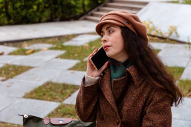 Sonbahar modasında giyinmiş ve telefonuyla internetten sohbet eden beyaz bir kadınla sakin bir şehir yürüyüşü.