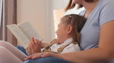 Sevgi dolu anne, çocuğuyla yatak odası ortamında yatarken yüksek sesle okur. Sakin bir aile ortamında çocukluk gelişimi ve dil gelişimi. Yan görünüm.