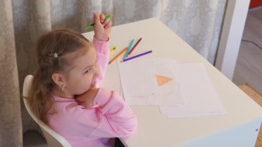 Beyaz bir kız, parlak bir odada masada oturup resim yapmayı öğreniyor. Anaokulu eğitimi ve sanat yoluyla yaratıcı erken çocukluk gelişimi kavramı. Üst görünüm.