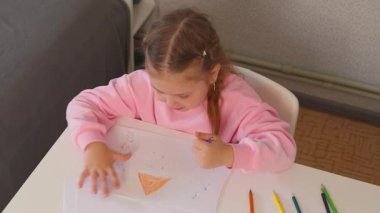 Genç kız çizimlerini parlak ve neşeli bir odada yapıyor. Okul öncesi eğitim ve erken çocukluk gelişimi. Yaratıcı öğrenmeye odaklı. Üst görünüm.