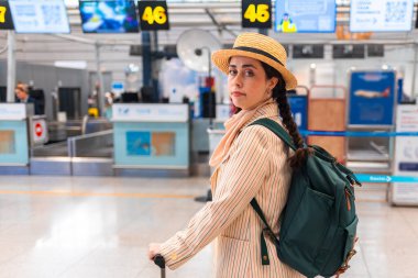 Zarif takım elbiseli, hasır şapkalı ve sırt çantalı bir kadın havaalanındaki kontrol gişesinin yanında duruyor. Uzayı kopyala Seyahat ve seyahat kavramı.