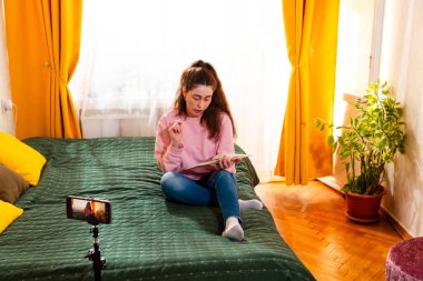 Influencer bir yatakta otururken bir vlog kaydediyor, seyircisini dijital pazarlama için ilham verici içerikle meşgul ediyor. Geniş açı, üst görünüm.