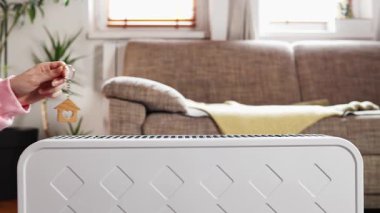 Kadın elinin kapağı elektrikli ısıtıcının üzerinde ev şeklinde anahtarlık gösteriyor. Uzayı kopyala Sıcak ev ve enerji krizi kavramı.