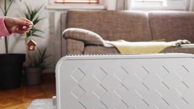 Kadının eli, elektrikli ısıtıcının üzerinde ev şeklinde anahtarlık gösteriyor. Uzayı kopyala Sıcak ev ve alternatif ısıtma sistemi kavramı.