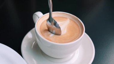 Köpüklü sıcak kahveyle yakın plan beyaz fincan, kaşıkla karıştırılmış. Kahvaltı için kapuçino ya da espresso.