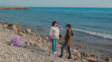 İki kadın aktivist bir plaj temizliğine katılarak kirliliği azaltmak için plastik atık topluyor. Gönüllüler bir fren yapıp çay içsin. Tam boy çekim.