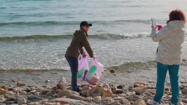 İki kadın eylemci, kirliliği önlemek ve doğayı korumak için plastik ve diğer döküntüleri toplayarak vahşi bir kıyı şeridini temizliyor. İnsanlar çevresel sorumluluk çabalarına katılıyorlar