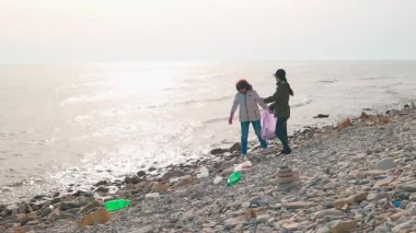 İki çevreci, kirlenmiş bir plajı, vahşi yaşamı korumak ve sahili restore etmek için plastik ve diğer döküntüleri toplayarak temizliyor. Okyanus temizliği ve sorumlu imha kavramı. Geniş açı.