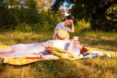 Mutlu orta yaşlı anne ve kızı yeşil bir çayırda tatildeler, dinleniyorlar ve iletişim kuruyorlar. Aile dinlenmesi ve psikolojik refah.