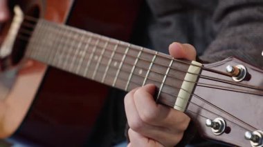 Gitar çalan bir kadının yakın çekimi. Parmaklar gitar boynundaki perdeleri kıskaçlıyor. Müzik aletleri çalmayı öğrenmek.