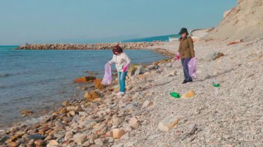 İki kadın eylemci deniz kıyısı boyunca çöp toplayarak kirlilik ve çevre temizliğinin önemi hakkında farkındalık yaratıyor. Okyanus koruması ve Dünya Günü konsepti. Geniş açı.