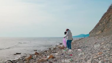 İki aktivist, kirliliği önlemek ve doğa koruma konusundaki farkındalığı artırmak için vahşi bir kıyı şeridinden çöp topluyor. İnsanlar daha temiz bir gezegen ve sürdürülebilir yaşam için harekete geçiyor. Geniş açı.
