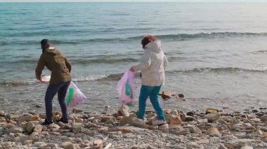 Eylemciler plajdan plastik atık ve çöp toplayarak kirliliği önlemeye yardım ediyorlar. İnsanlar doğayı temizlemek ve korunma hakkında farkındalık yaratmak için harekete geçiyor. Tam boy çekim.