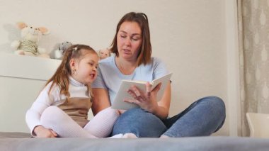 Bakıcı, küçük bir kızın ilk kitabını parlak bir odada okumasına yardım eder. Anaokulu ve çocuk gelişimi kavramı. Alt görünüm.