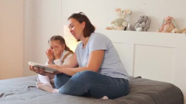Küçük çocuk annesinin yanında oturup kitap okurken onu takip eder. Erken çocukluk edebiyatı ve duygusal destek. Geniş açı.