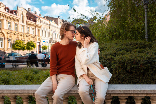 Young Caucasian couple relax in park sitting on ballustrade. Romantic date in Valentine's Day.