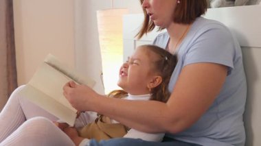 Genç bir kadın kızıyla yatakta sakin bir okuma anını paylaşıyor. Eğitimsel bağ ve konuşma geliştirme, kapalı alanda gevşeme sırasında. Orta çekim