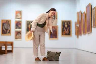 Çağdaş bir sanat sergisini ziyaret ederken genç, beyaz, zarif bir kadının geniş bir görüntüsü başını tutuyor. Resimler arka planda. Müze Günü kavramı.