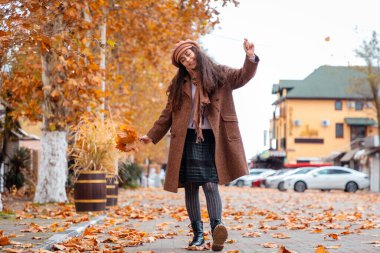 Rahat bir palto ve bereye sarılmış beyaz bir kadın sonbahar sokaklarında dans ederek boş zamanlarının ve huzurlu şehir ortamının tadını çıkarıyor.