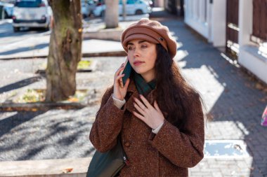 Beyaz bir kadının portresi. Paltolu ve bereli güzel bir kadın. Sokakta akıllı bir telefondan arıyor. Üst görünüm.